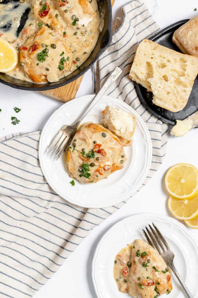 Chicken with a lemon butter sauce on a plate with crusty bread and the pan of chicken piccata.