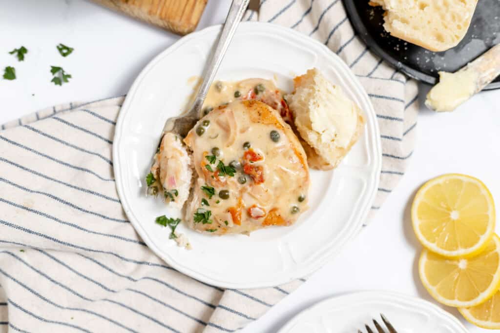 A serving of easy chicken piccata served with a piece of bread and sliced lemons.