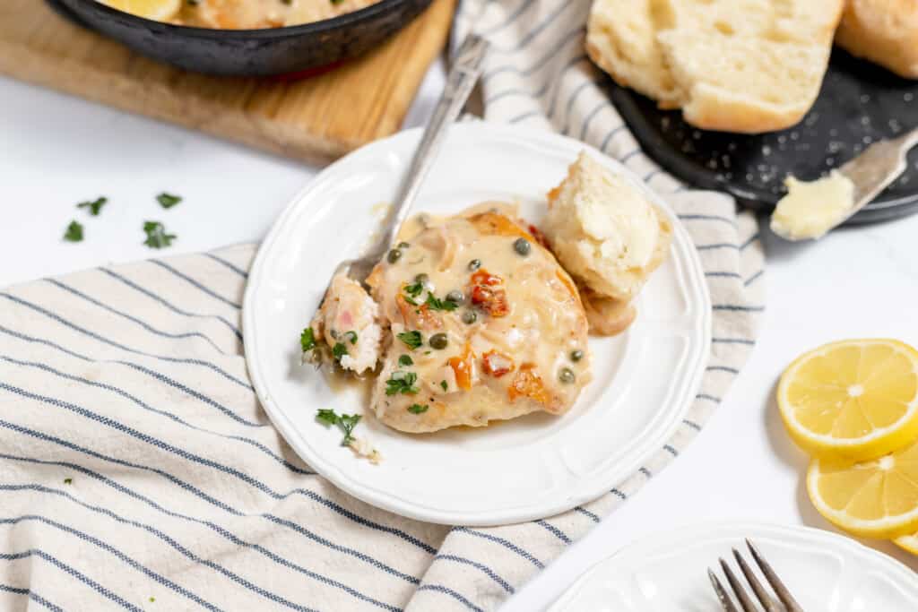 A serving of easy chicken piccata served with a piece of bread and slices of lemons.