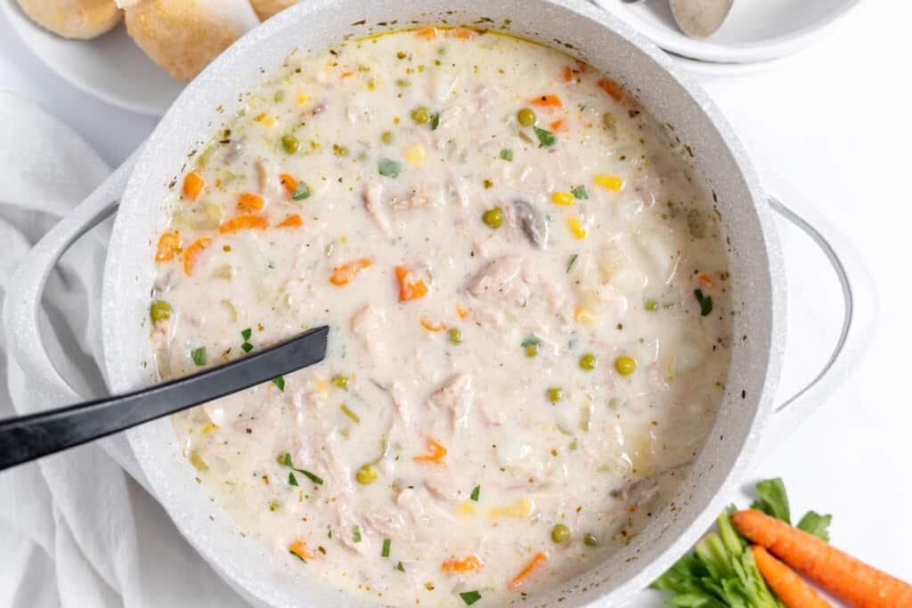 A big pot of chicken pot pie soup with a ladle.