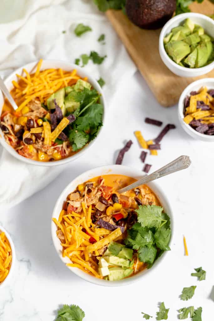 Big bowls of taco soup with toppings and spoons, with bowls of toppings in the background.
