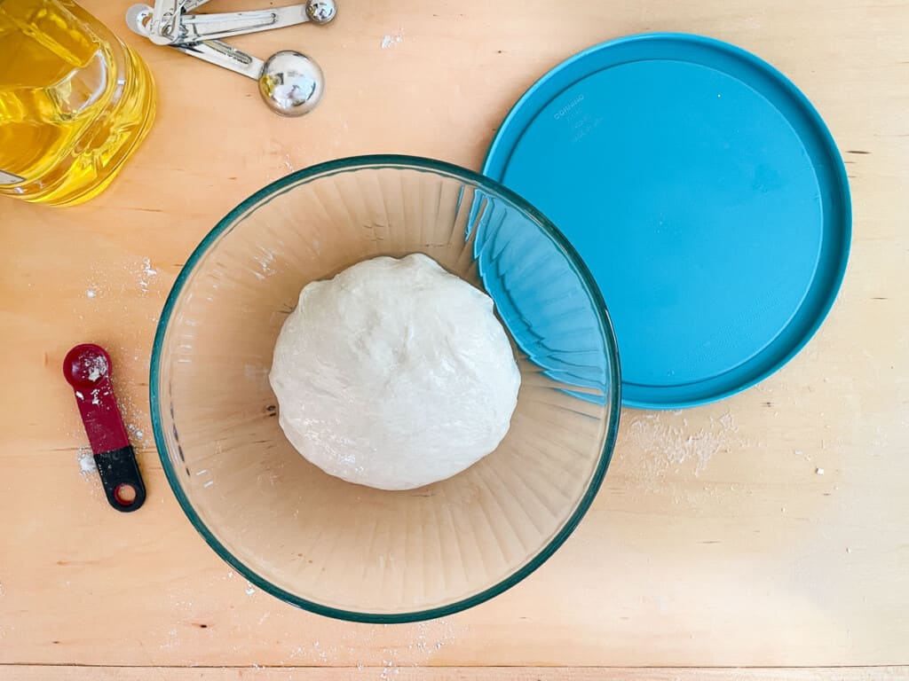 Greased bowl with dough ready to rise, with oil, measuring spoons and the bowl lid.