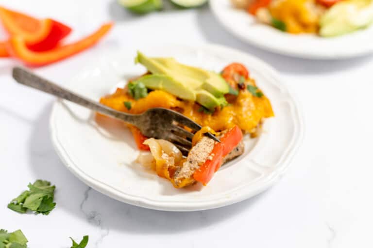 A serving of chicken fajita casserole accompanied by a side bowl of shredded cheese, fresh cilantro, and sliced limes for garnishing.
