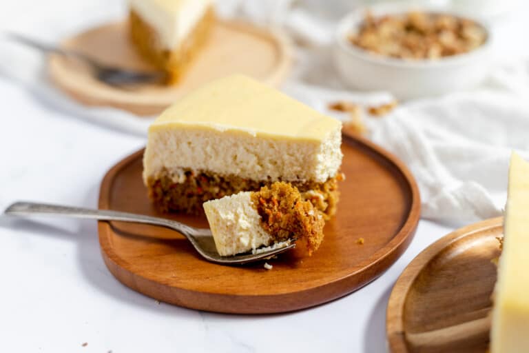 A bite of 2/1 double decker carrot cake cheesecake with the rest of slices in the background.