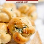 Close-up of golden brown Garlic Knots topped with parsley and grated cheese on a wooden board, with the text "Garlic Knots: Always a Hit" above.