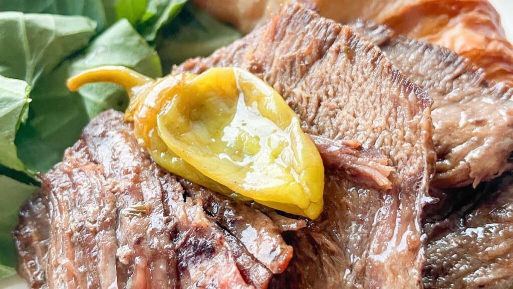 Close-up of grilled Mississippi pot roast topped with a yellow pepper slice, accompanied by green spinach leaves.