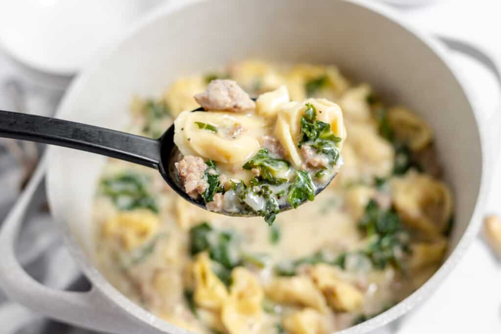 A ladle full of creamy sausage tortellini soup.