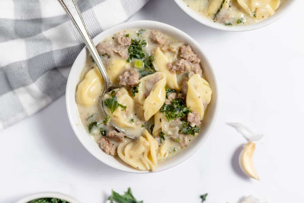 A bowl of sausage tortellini soup with a spoon on it.