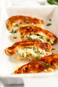 Stuffed chicken breast filled with cream cheese and spinach in a white baking dish.