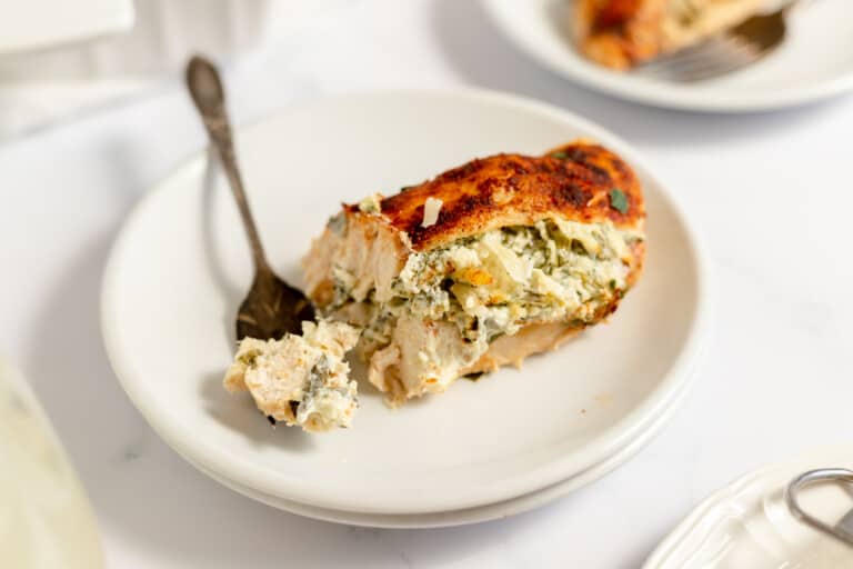 A piece of stuffed chicken breast with a creamy spinach filling on a white plate beside a fork, with a white background.