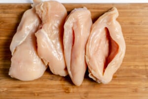 Chicken breast cut for stuffing on a wooden cutting board.