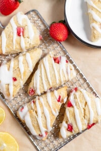 Strawberry Scones with lemon glaze on a wire rack with strawberries and lemon slices.