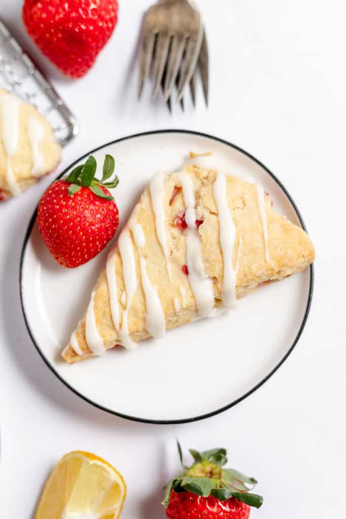 One perfect scone on a plate with fresh fruit around it.