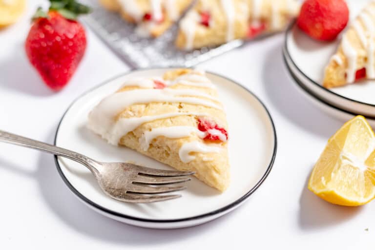 A strawberry scone on a plate with berries and lemons.