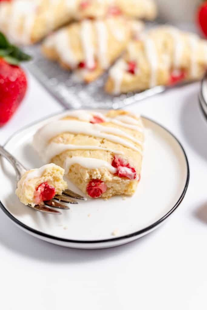 A fork with a bite of scone on it and a scone cut apart on the plate.