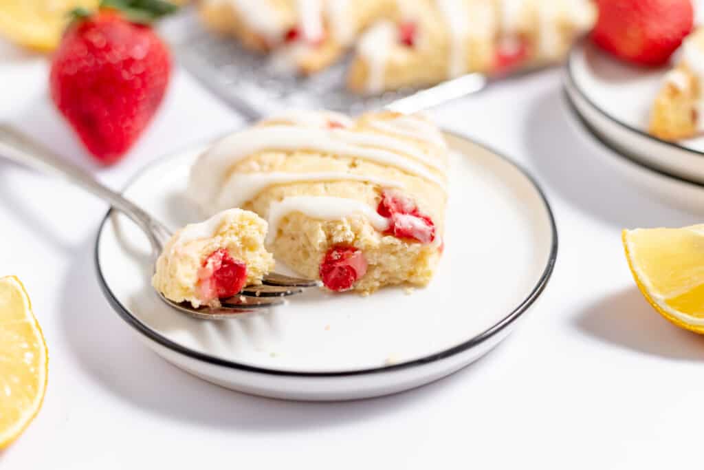 A plate with sliced strawberry scones topped with glaze, next to fresh strawberries.