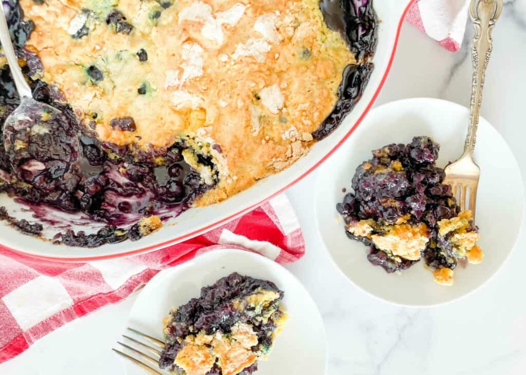 Two plates of blueberry dump cake and the pan of dump cake.