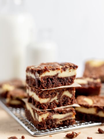 Swirled cheesecake brownies stacked up on a cooling rack.