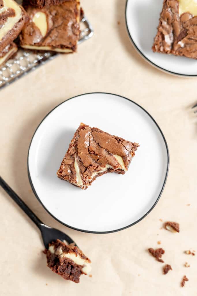 Overhead shot of a brownie on a plate with a fork and more brownies around it. 