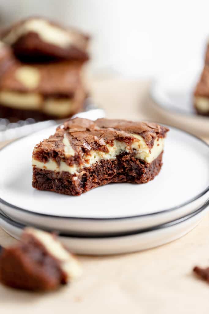 A cheesecake brownie on a plate with a bite taken out of it. 