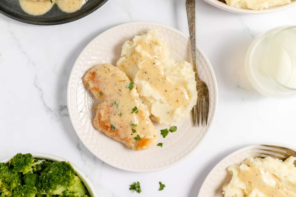 Top down shot of a dinner table with a plate of creamy ranch chicken, broccoli, and dinner plates.