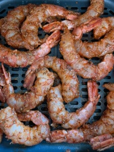 Uncooked shrimp in the basket of the air fryer ready to cook.
