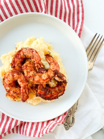 A plate with blackened shrimp, polenta, a striped towel, and a fork.