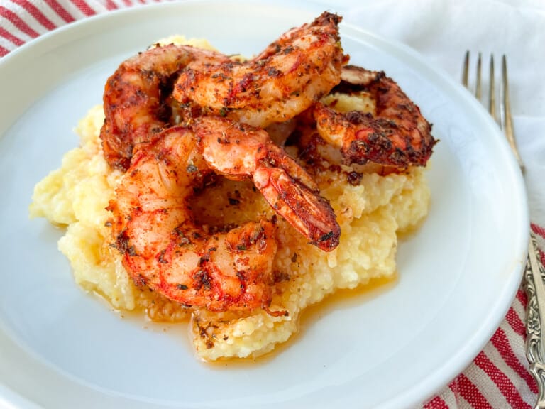 Blackened Shrimp on top of polenta on a white plate.