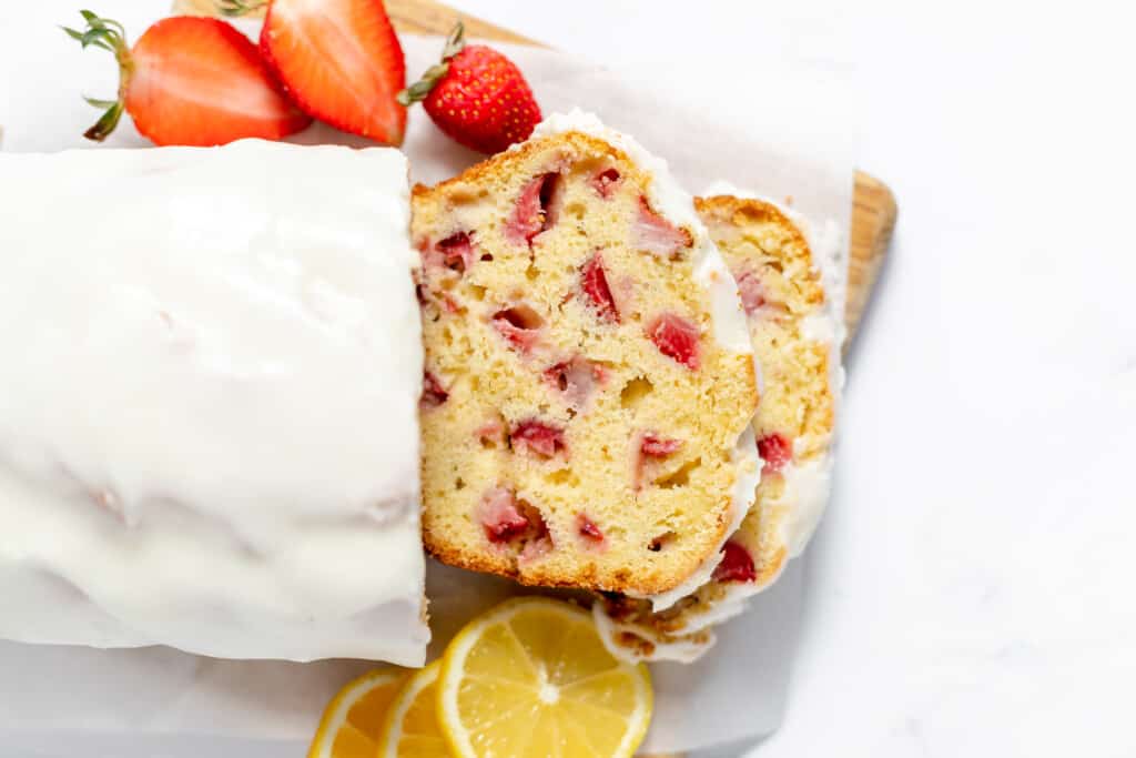 Fresh strawberry bread sliced on a cutting board with lemons and berries.