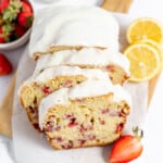 Iced strawberry loaf with lemons and berries on a cutting board.