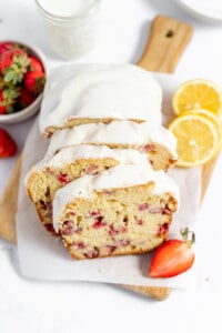 Iced strawberry loaf with lemons and berries on a cutting board.