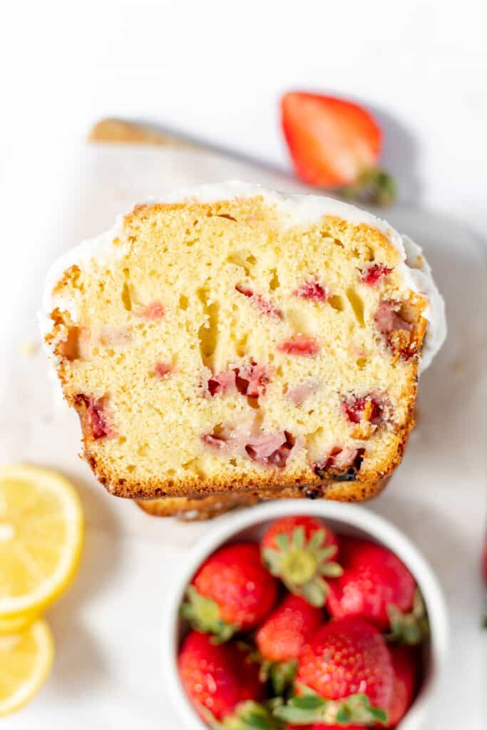 A slice of strawberry bread with fresh berries and lemon next to it.