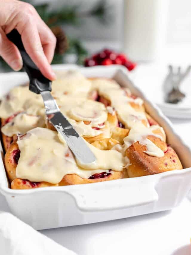 A person cutting a cranberry cinnamon roll in a white dish.