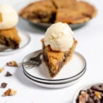 Front end view of a chocolate chip pie with vanilla ice cream on a plate with the pie in the background.