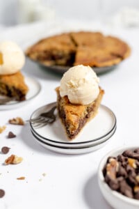 Front end view of a chocolate chip pie with vanilla ice cream on a plate with the pie in the background.