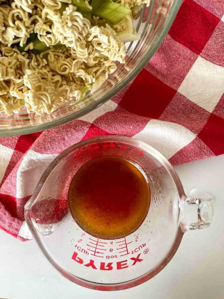 Ramen Salad with the salad dressing on a counter with a red and white linen. 