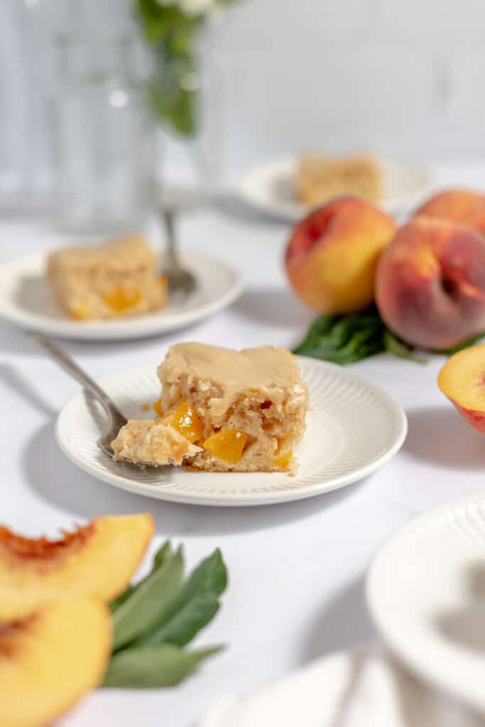 Peach cake on a plate with fresh peaches around it. 