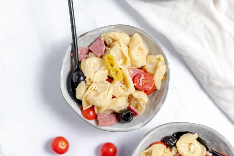 A close up of tortellini salad in a bowl with a spoon.