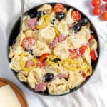 A large bowl of tortellini salad on a tablecloth with parmesan cheese and tomatoes on the side.