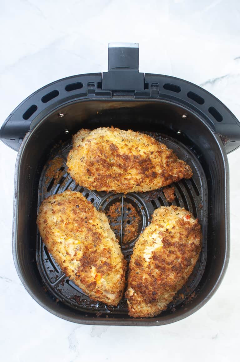 Stuffed chicken breasts in the basket of an air fryer.