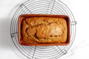 Baked quick bread in a loaf pan on a cooling rack.