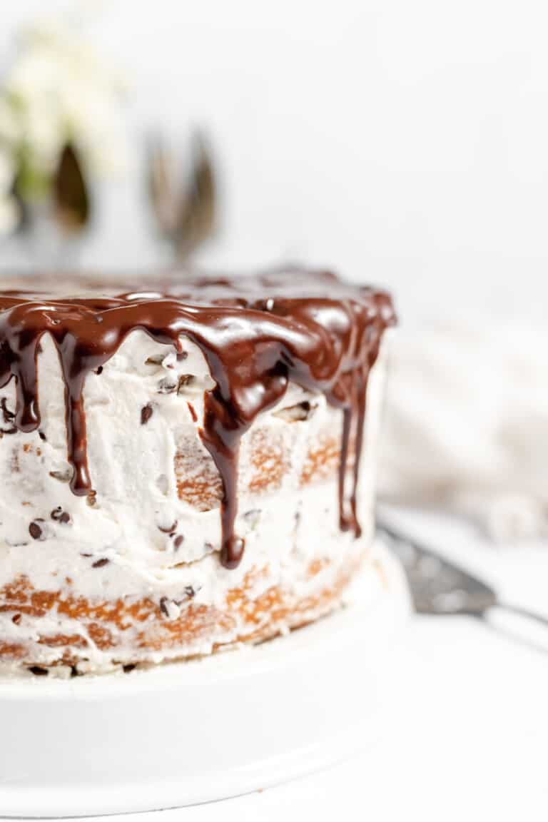 Cannoli Cake with 3 layers, frosting, filling, and chocolate ganache, with a slice cut out of it and a piece of cake on a plate.
