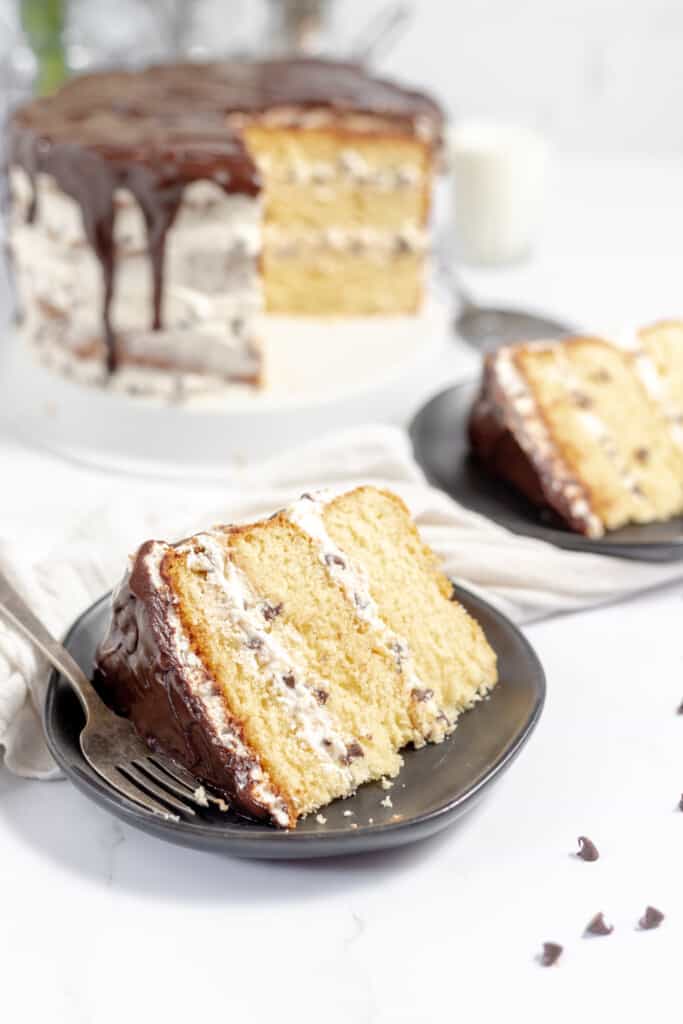 2 Slices of cannoli cake with the cake on a cake stand with mini chocolate chips.