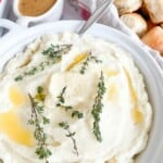 A bowl of mashed potatoes with gravy and rolls.
