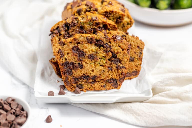 Sliced chocolate chip zucchini bread on a platter and white linens.