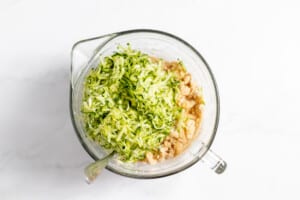 Shredded zucchini added to batter in a bowl.