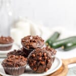 Double chocolate muffins with zucchini piled on a plate with milk in the background and zucchini next to it.
