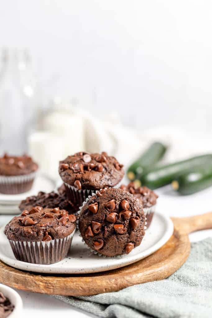 Double chocolate muffins with zucchini piled on a plate with milk in the background and zucchini next to it. 