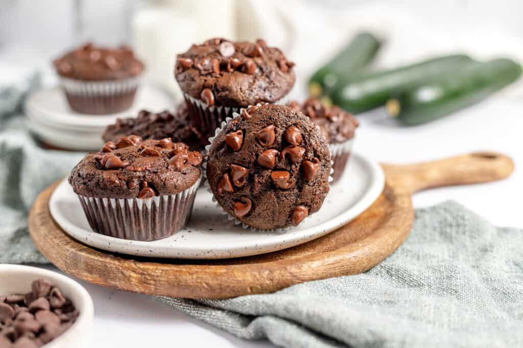 Double chocolate zucchini muffins on a plate with zucchini in the background. 