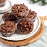 A pile of chocolate zucchini muffins on a white plate on a cutting board.